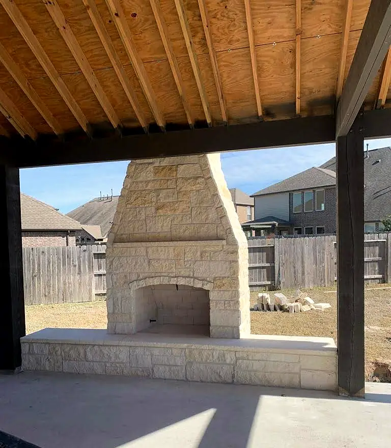Chopped limestone outdoor fireplace with a raised hearth under a covered patio