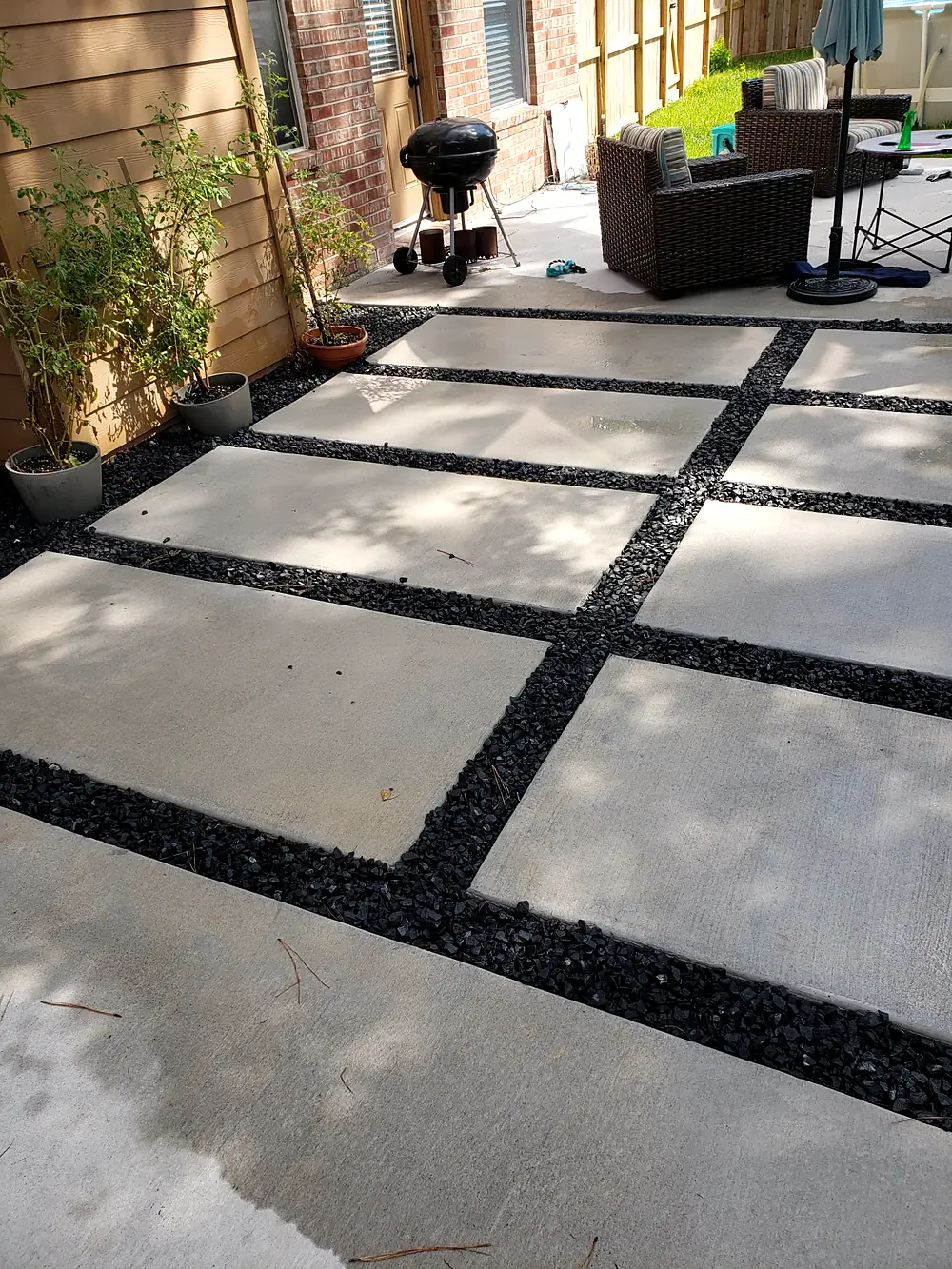 Large concrete pads separated by black gravel along a brick house