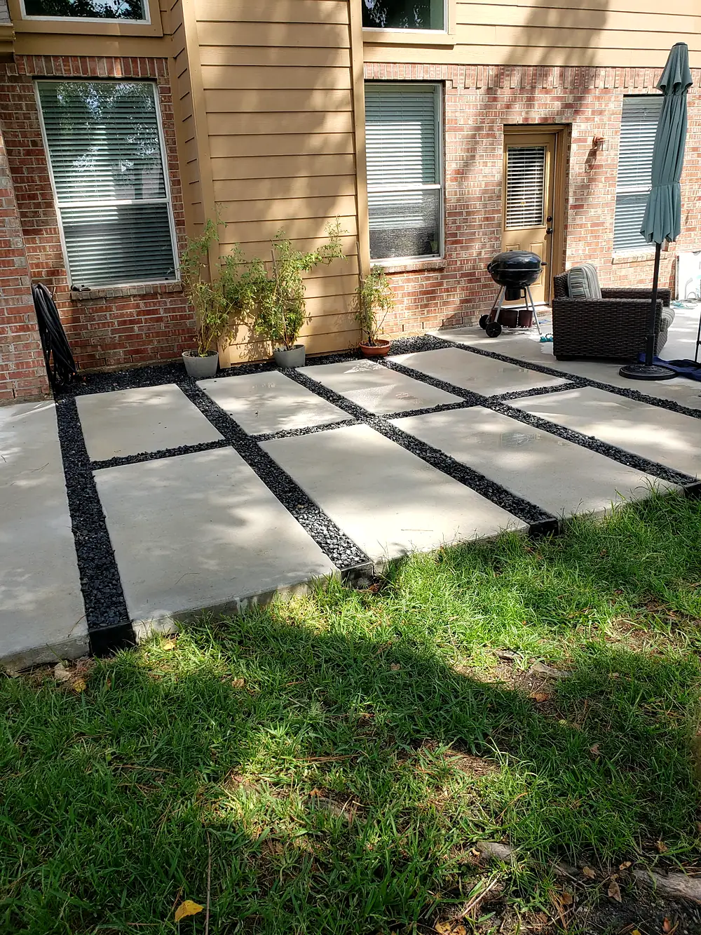 Modern patio of large concrete pads separated by black gravel behind a brick house