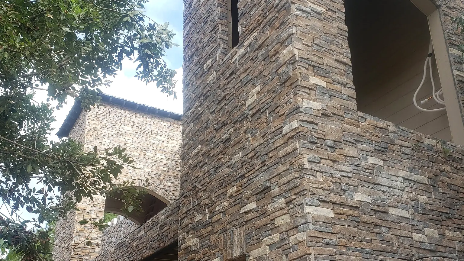 Building with a stone tower and arched balconies, clad in stacked stone